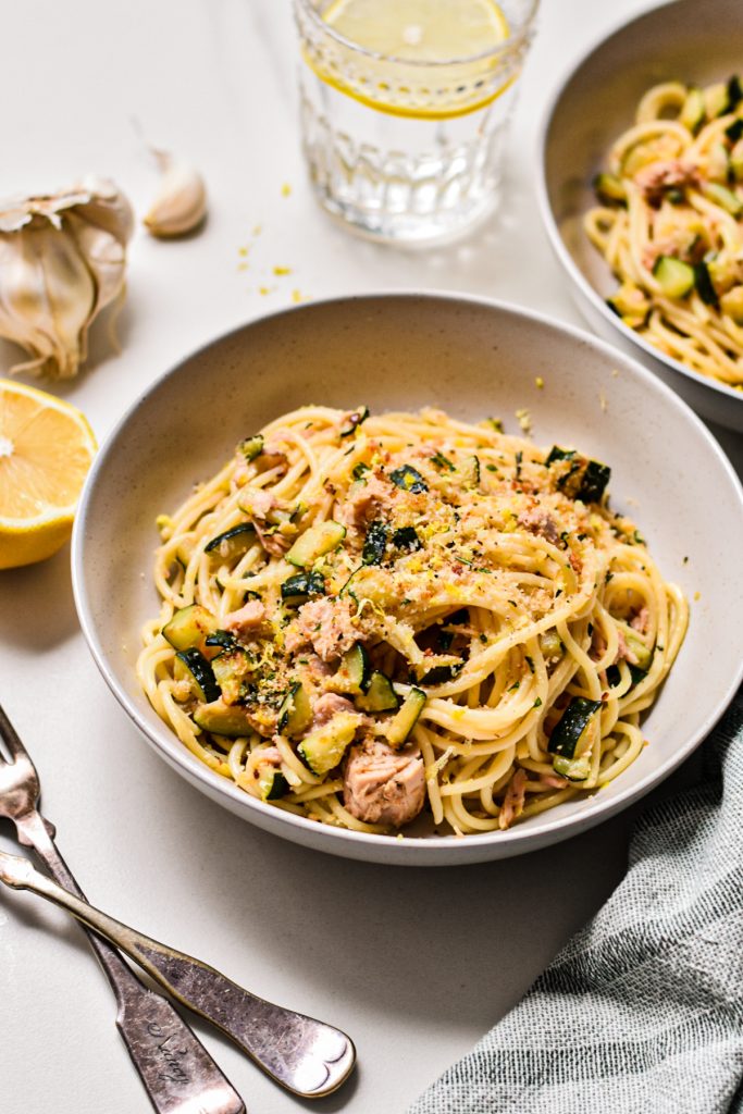 White bowl served with zucchini tuna pasta with lemon on the side.