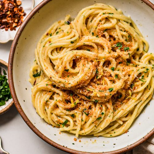 Swirled spaghetti pasta in a bowl topped with breadcrumbs and fresh parsley.