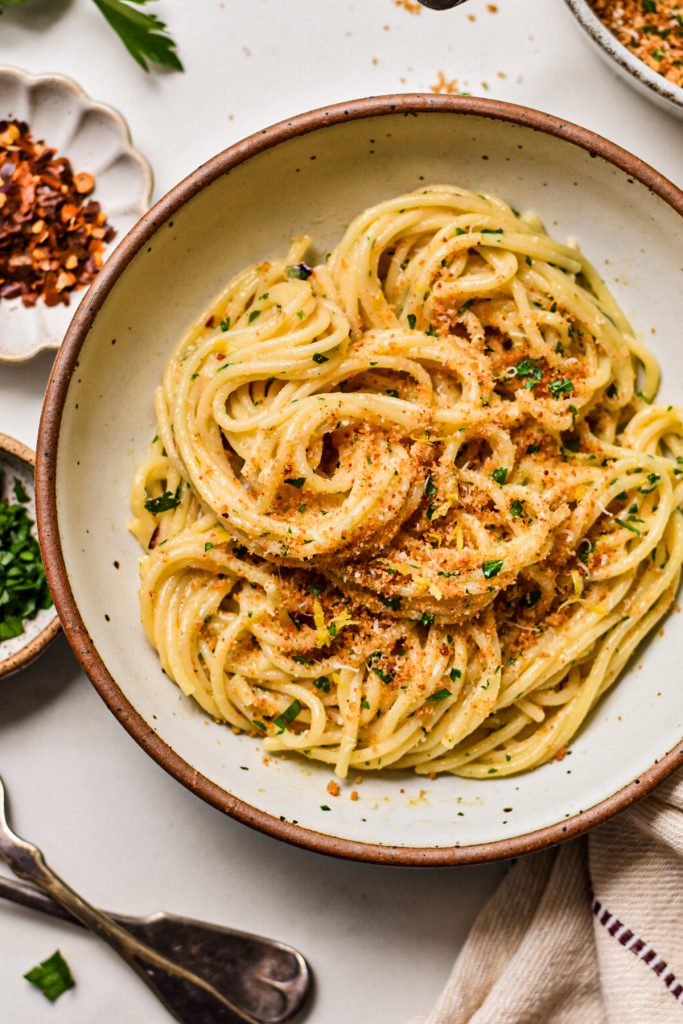 Swirled spaghetti pasta in a bowl topped with breadcrumbs and fresh parsley.