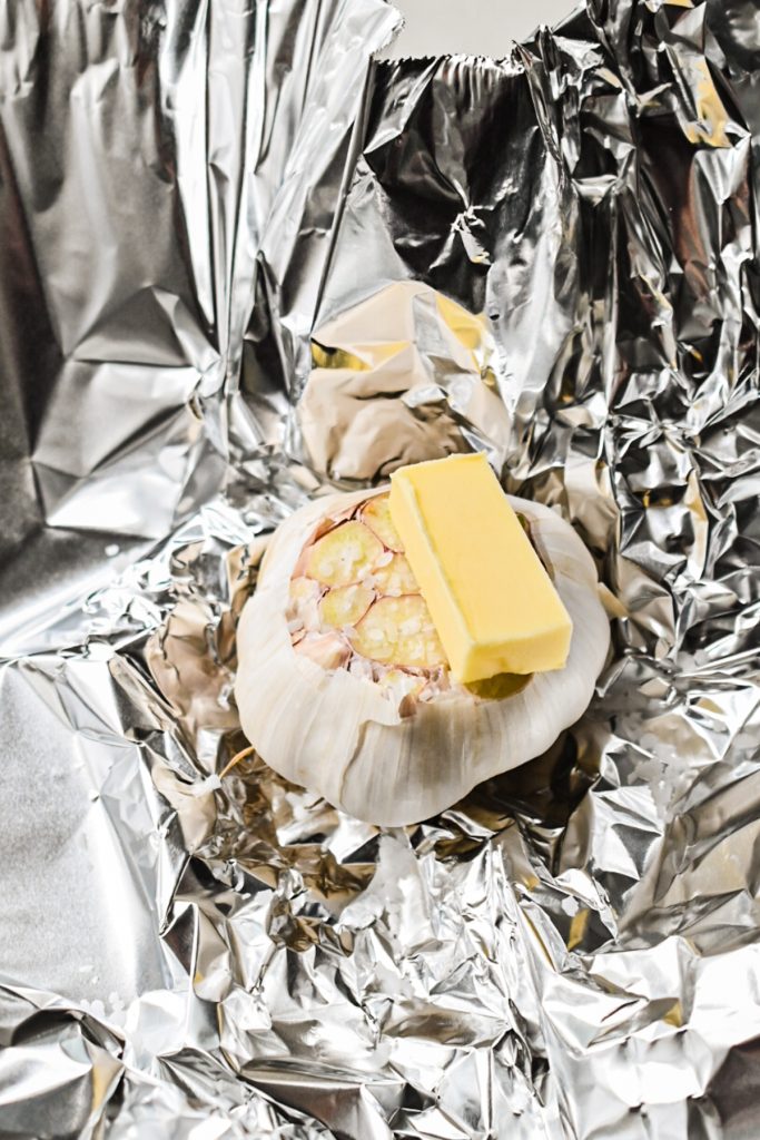 Raw head of garlic with butter on top in foil.