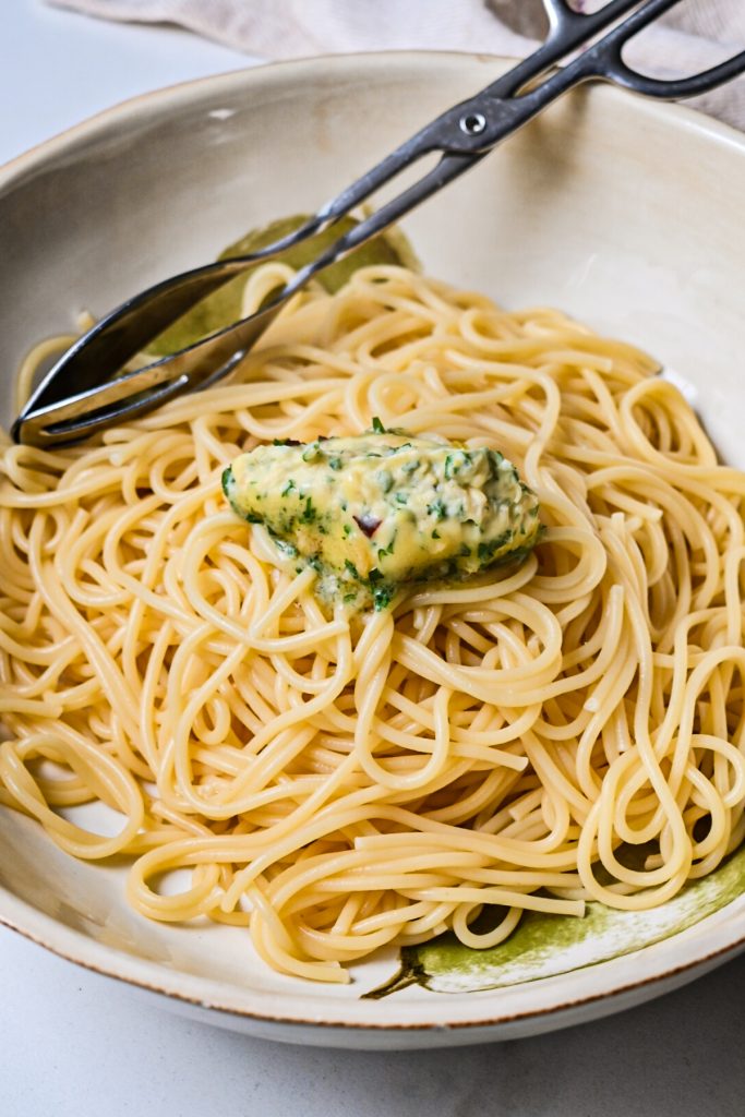 Adding the compound butter to a bowl of freshly cooked spaghetti.