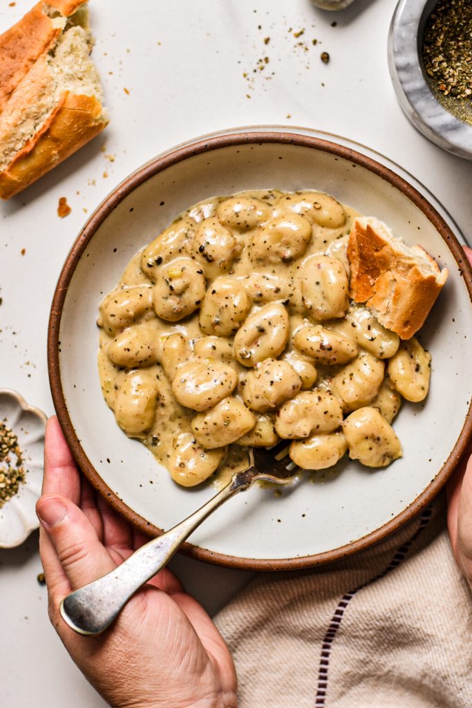 Hands holding a bowl of gnocchi au poivre served with bread.