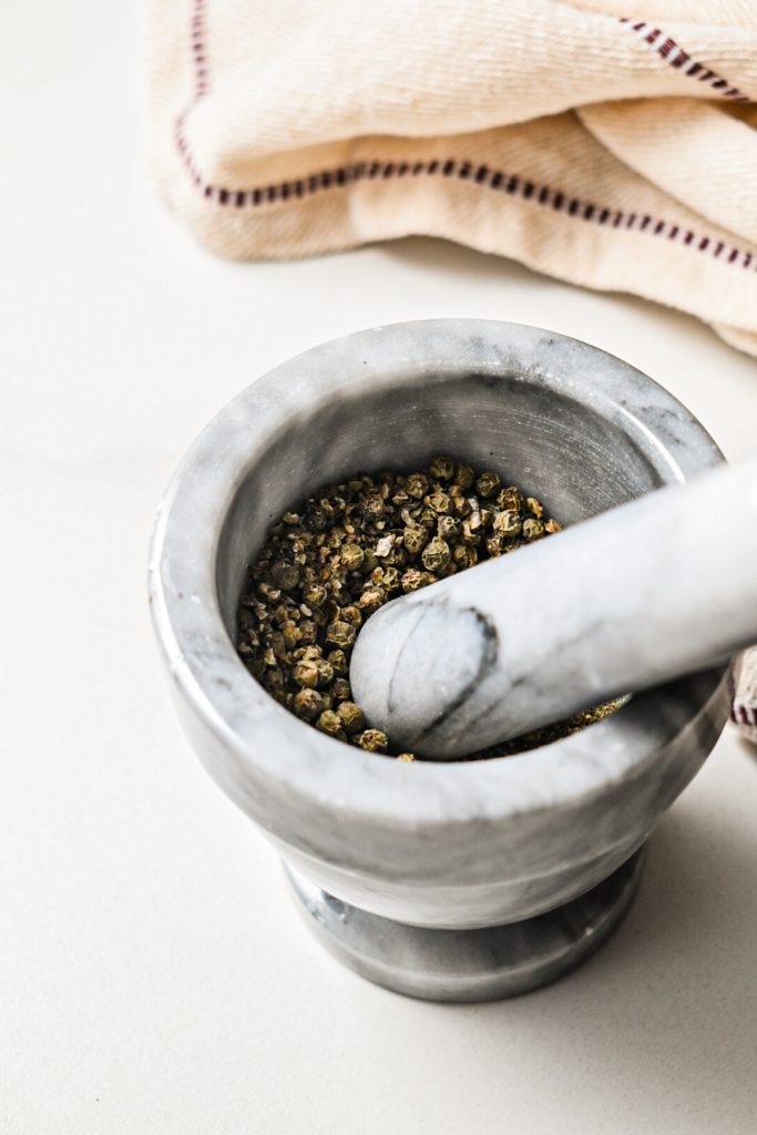 Whole peppercorns in a mortar and pestle to be crushed.