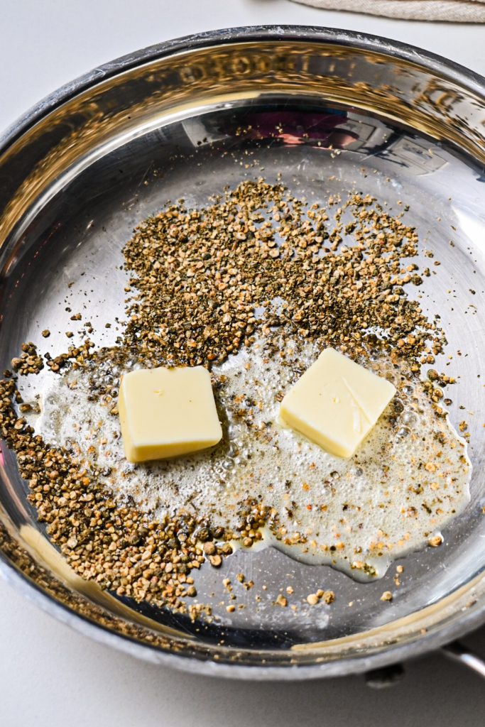 Crushed peppercorns in a pan with two squares of butter.