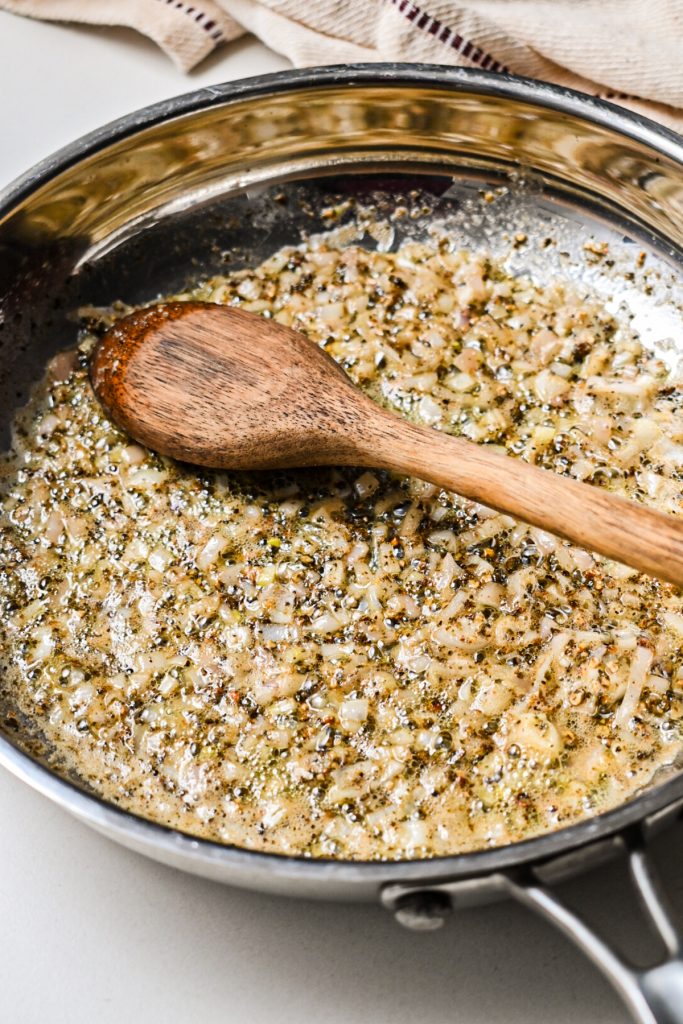 Butter, peppercorn and shallots cooking in a pan with a wooden spoon.