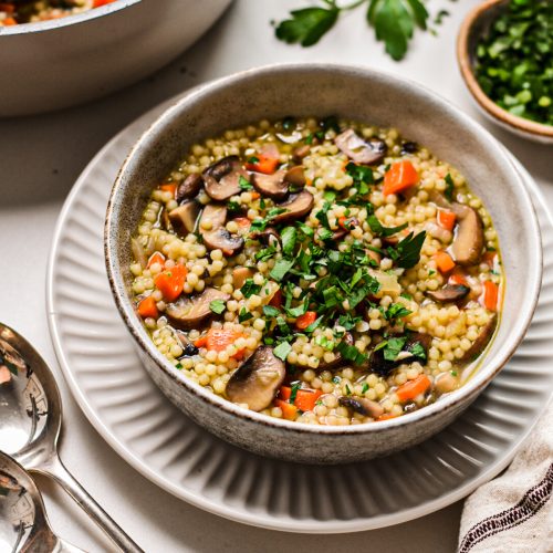 Bowl of mushroom soup with acini di pepe garnished with fresh parsley.