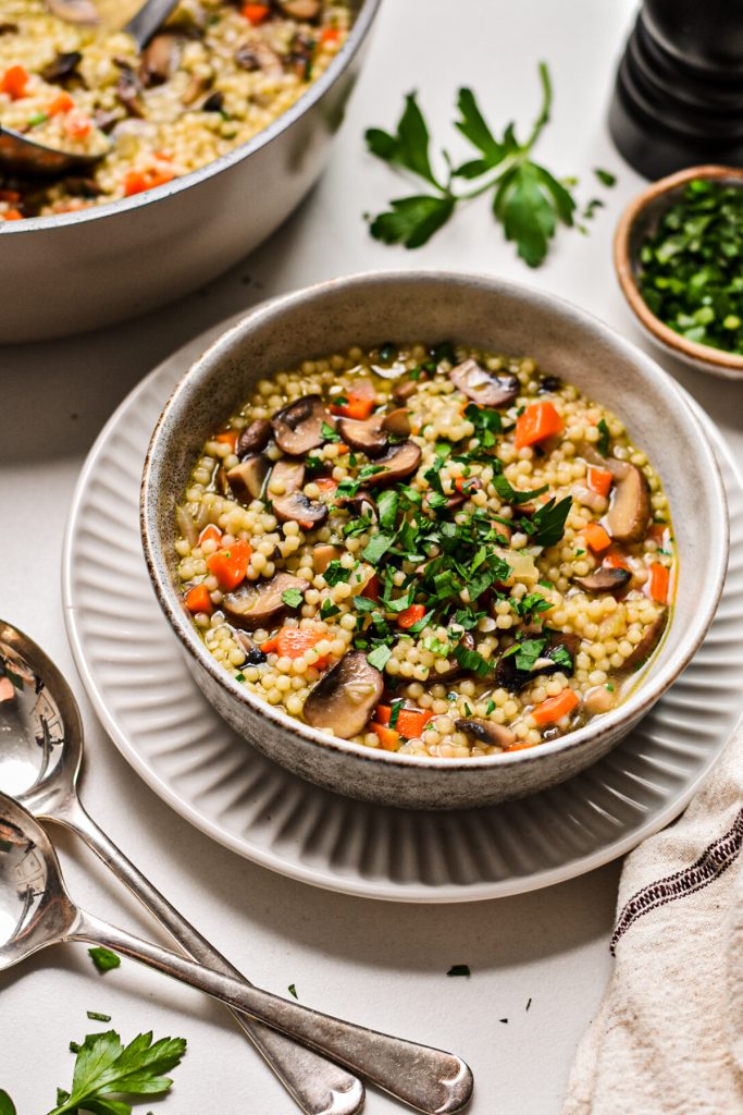 Bowl of mushroom soup with acini di pepe garnished with fresh parsley.