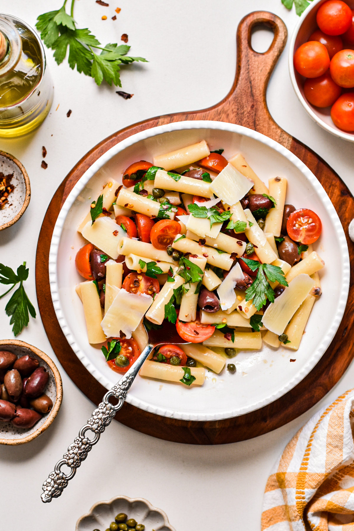 Puttanesca pasta salad in a serving bowl on a round wooden board.