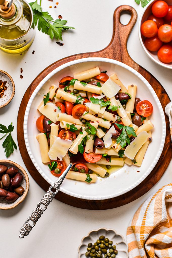Large serving bowl with puttanesca pasta salad topped with shaved parmesan.