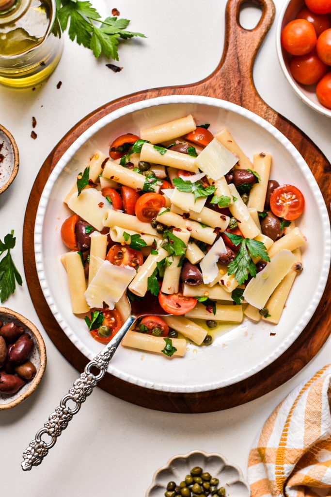 Puttanesca pasta salad served in a large bowl topped with shaved parmesan.