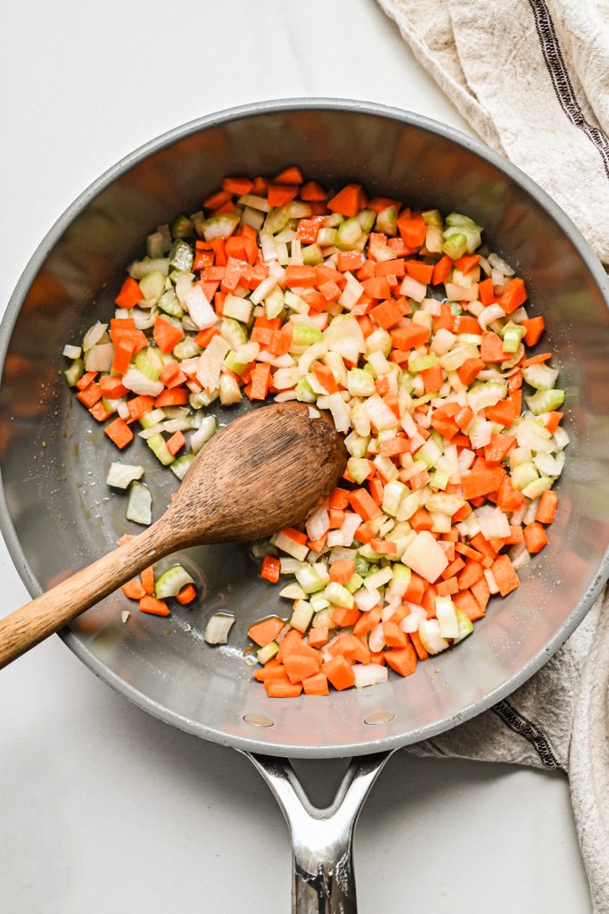 Overhead shot of diced onions, celery and carrots in a large pot with a wooden spoon.