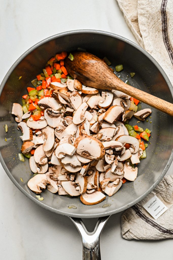 Chopped mushrooms added to the sauteed veggies in a pot.