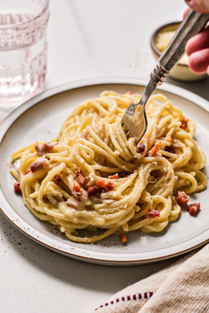 Fork swirling noodles from the plate of pancetta cauliflower pasta.