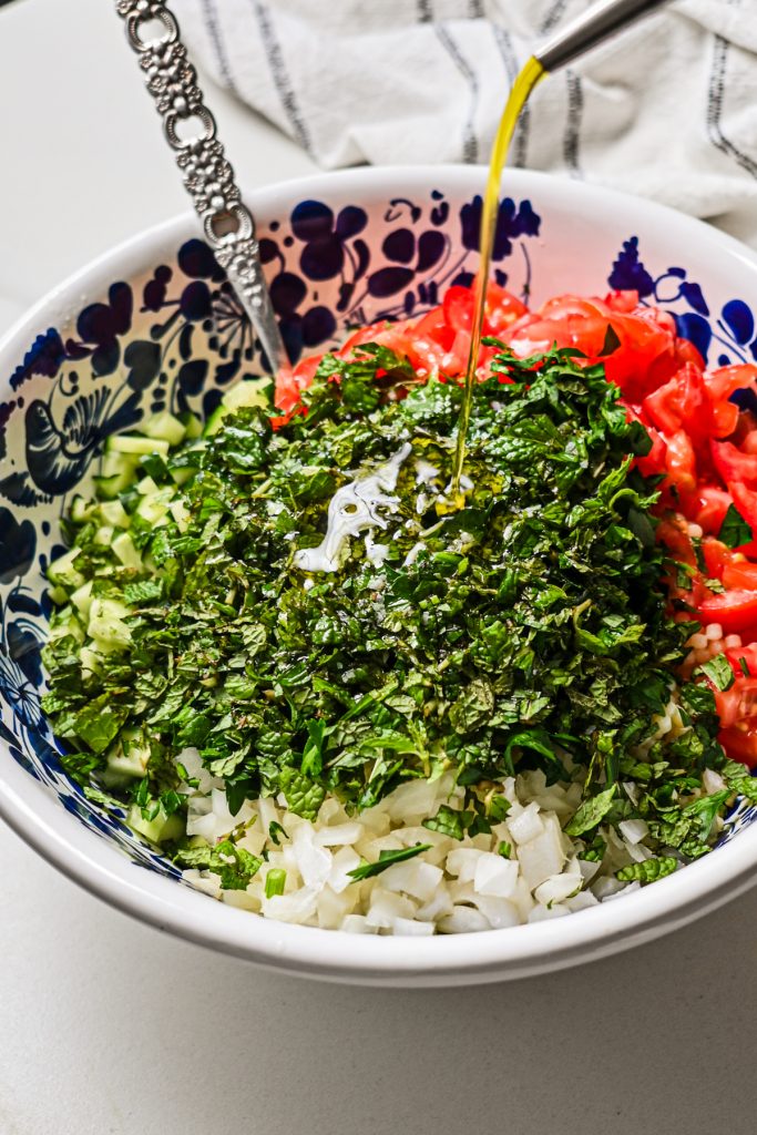 Drizzling olive oil into the tabbouleh salad in a large bowl.