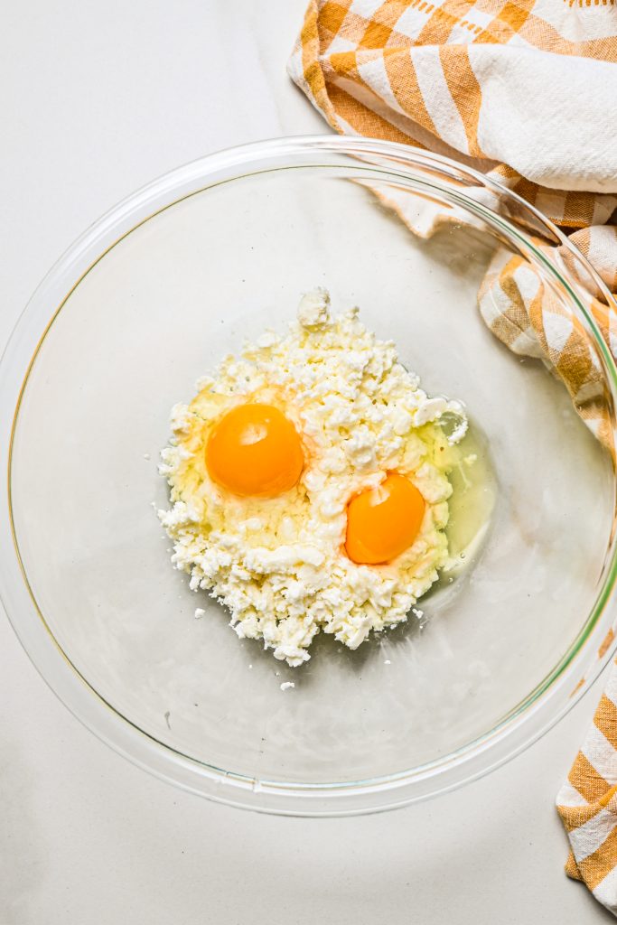 Crumbled feta cheese with eggs in a glass mixing bowl.