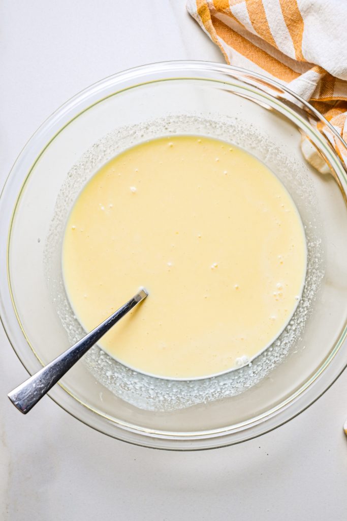 Milk, eggs, feta, salt and pepper mixed together with a fork in a glass mixing bowl.