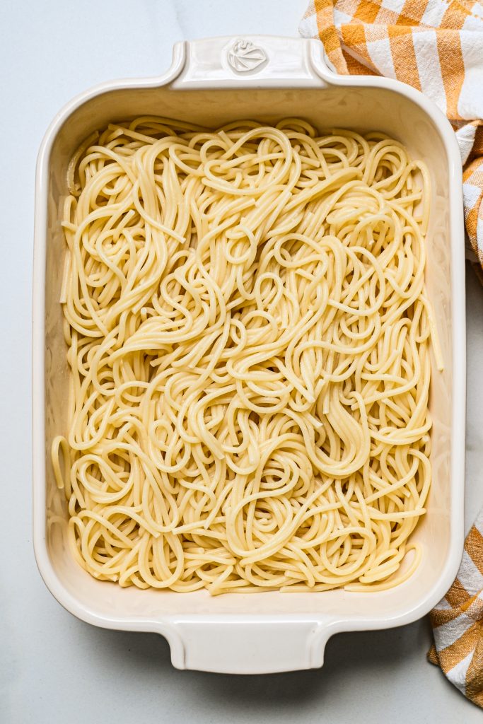 Cooked spaghetti noodles in the bottom of a white baking dish.
