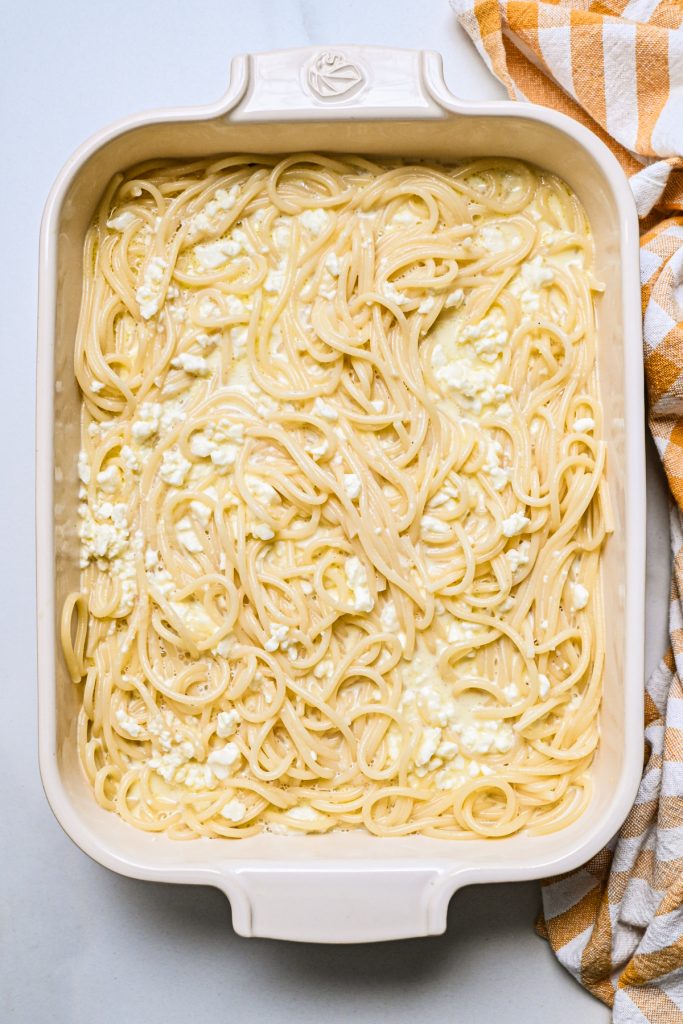Feta, milk and egg mixture poured over the top of the cooked spaghetti in a baking dish.