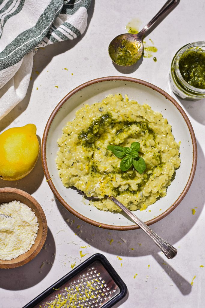 Overhead shot of creamy pesto pastina in a bowl next to the toppings.