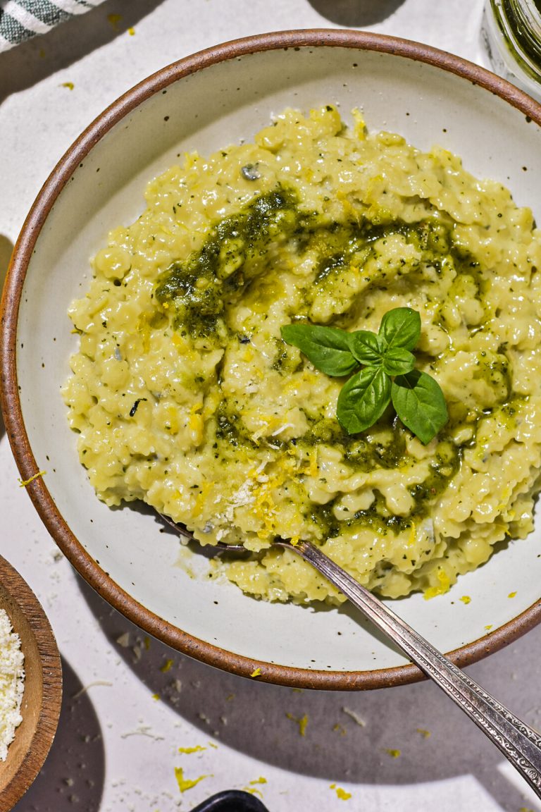 Close up of creamy pesto pastina in a bowl drizzled with extra pesto and fresh basil on top.