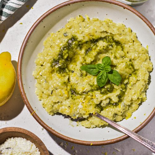 Creamy pesto pastina with gorgonzola cheese in a shallow speckled bowl with a spoon.