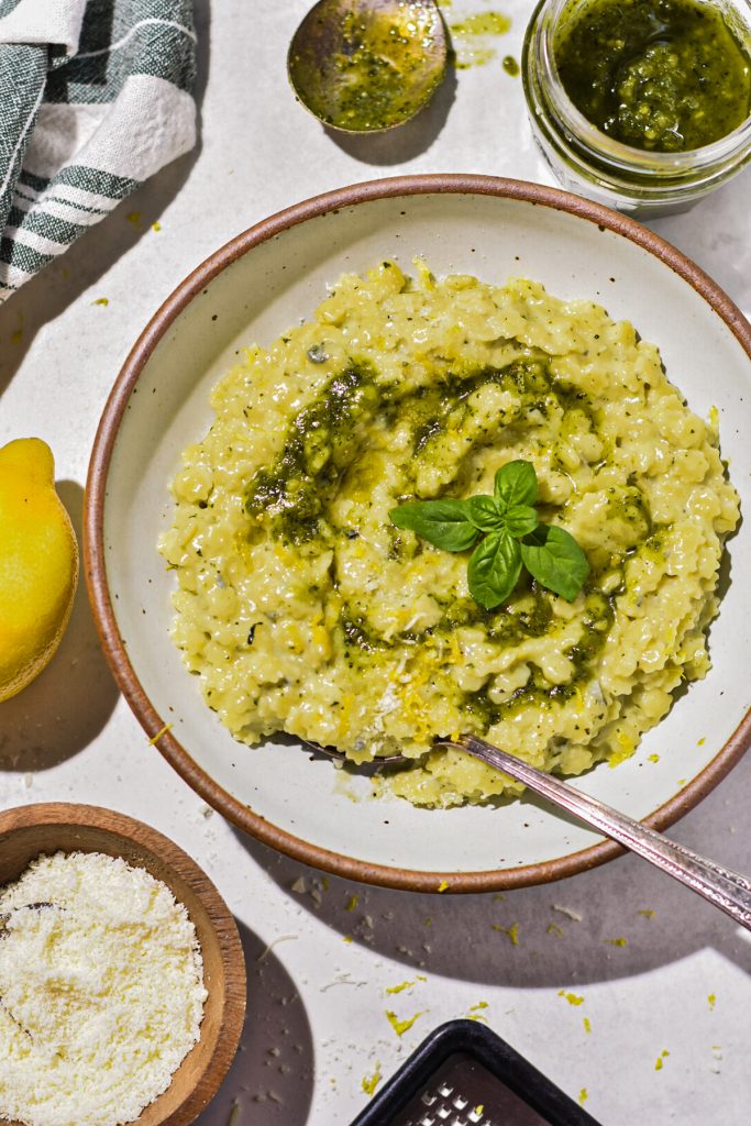 Creamy pesto pastina with gorgonzola cheese in a shallow speckled bowl with a spoon.