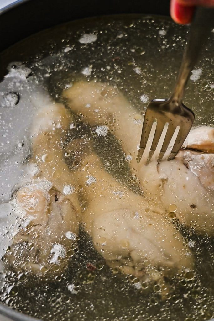 Chicken legs simmering in water in a large pot.