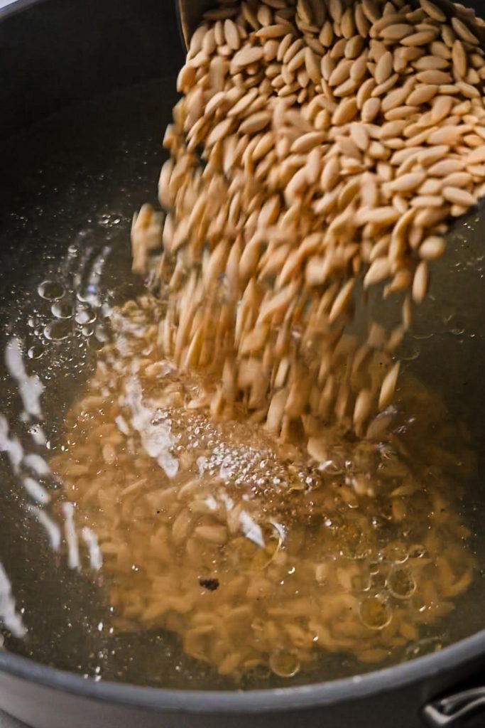 Adding orzo to the water in a large pot.