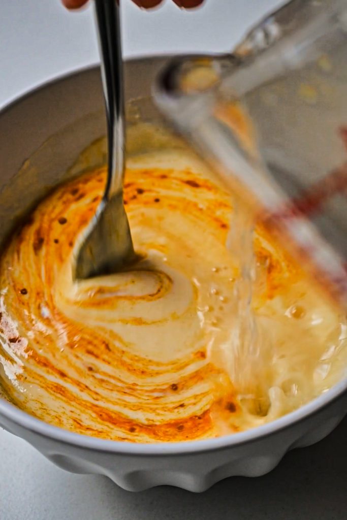 Mixing together turmeric, yogurt, egg, and lemon juice with a little bit of hot broth.