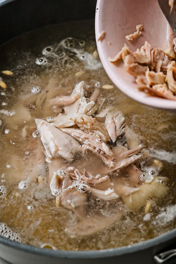 Adding shredded chicken back into the pot of soup with orzo.