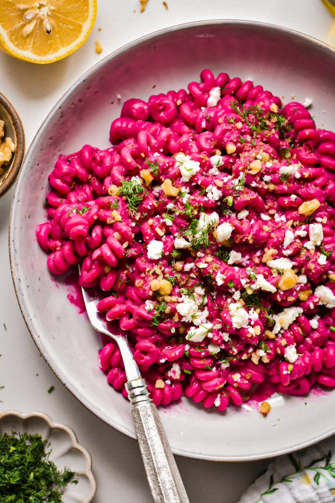 Close up of creamy chickpea beet pasta in a shallow pasta bowl with a fork.