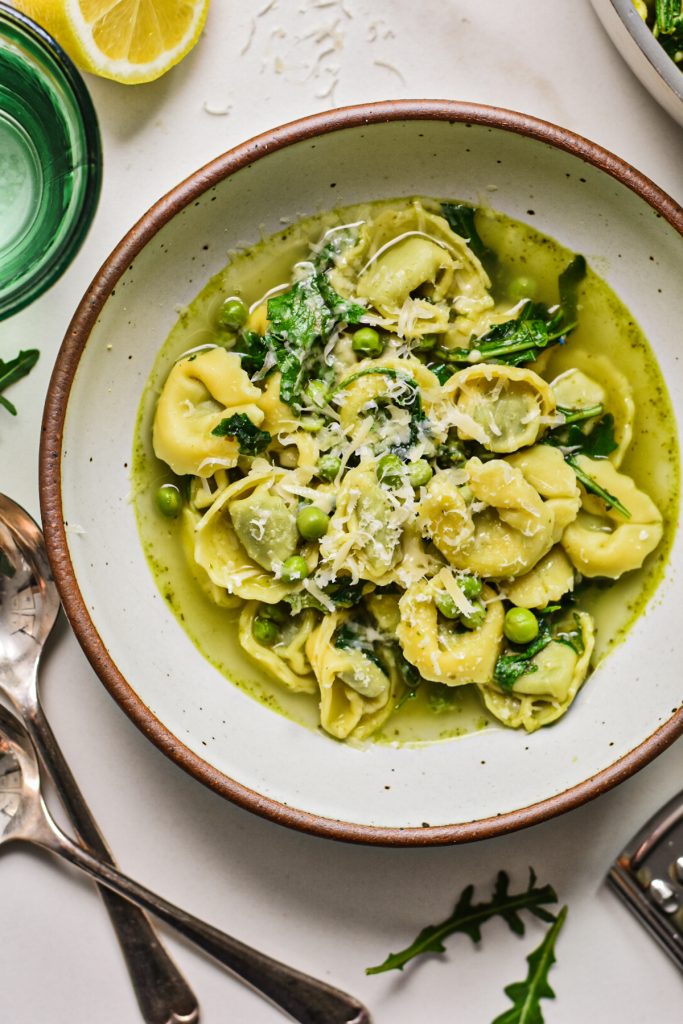 Overhead shot of spring tortellini in brodo served in a bowl with parmesan on top.