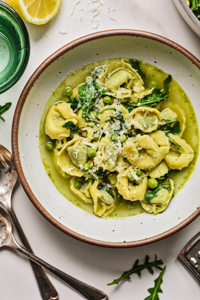 Overhead shot of spring tortellini in brodo served in a bowl with parmesan on top.