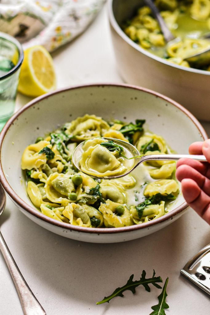 Spoon scooping up a bite of spring tortellini in brodo from a bowl.