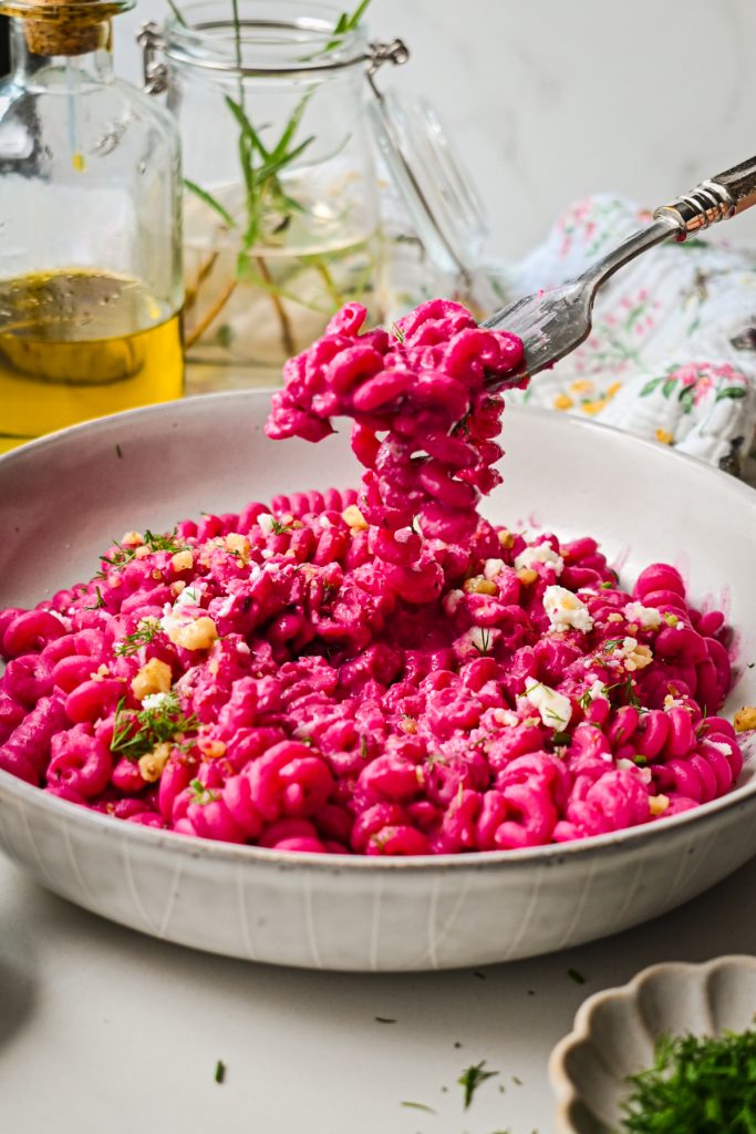 Fork pulling up some beet pasta from a bowl of pasta.