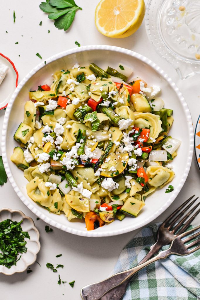 Grilled veggie tortellini pasta salad in a white serving bowl topped with feta.