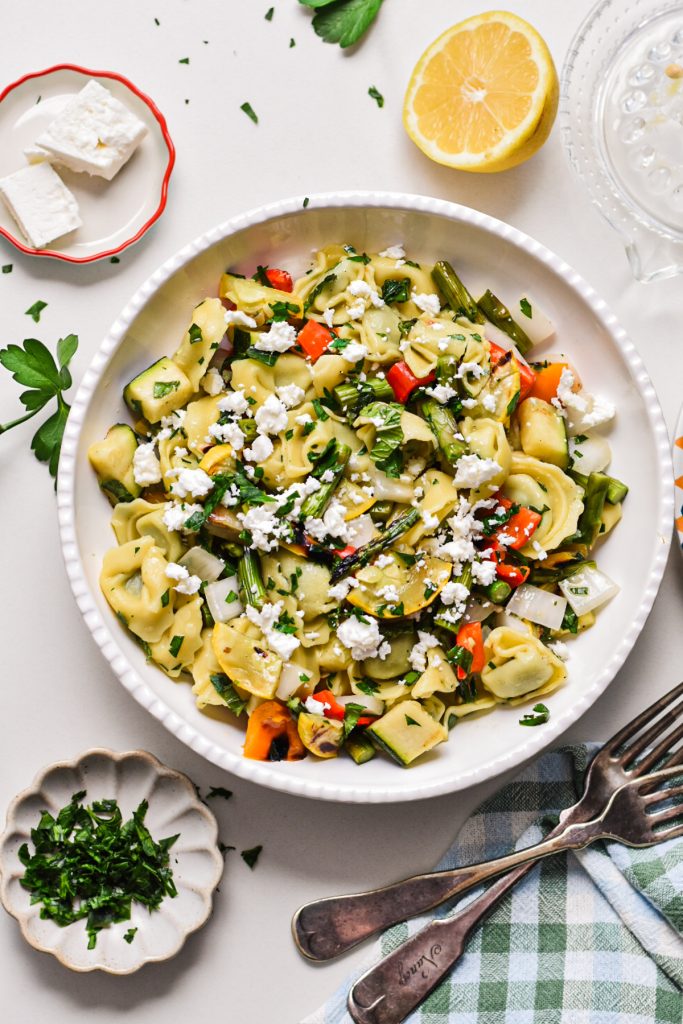Overhead shot of grilled vegetable tortellini pasta salad in a bowl with fresh herbs on top.