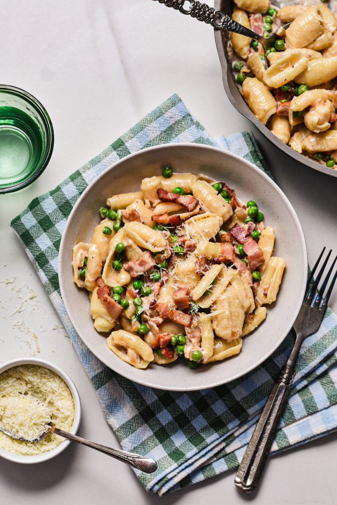 Creamy barilotti pasta with bacon and peas in a bowl on a plaid linen.