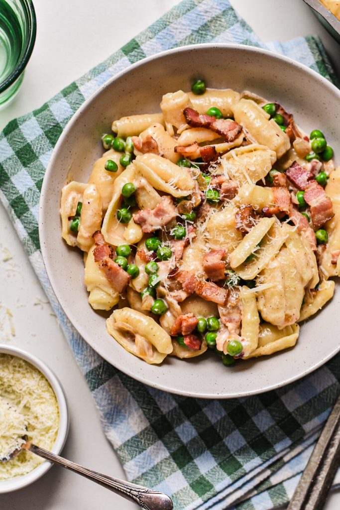 Close up of creamy barilotti with bacon and peas in a bowl topped with parmesan.