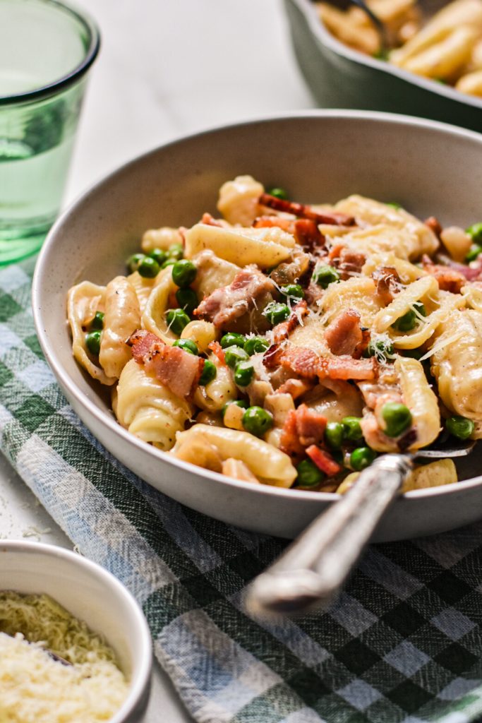 Side view of a bowl of creamy barilotti with bacon and peas.
