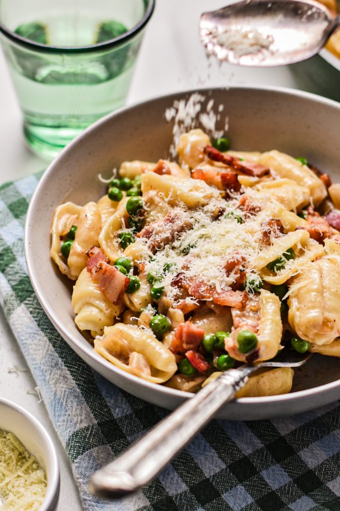 Sprinkling parmesan cheese on top of the creamy barilotti pasta in a bowl.