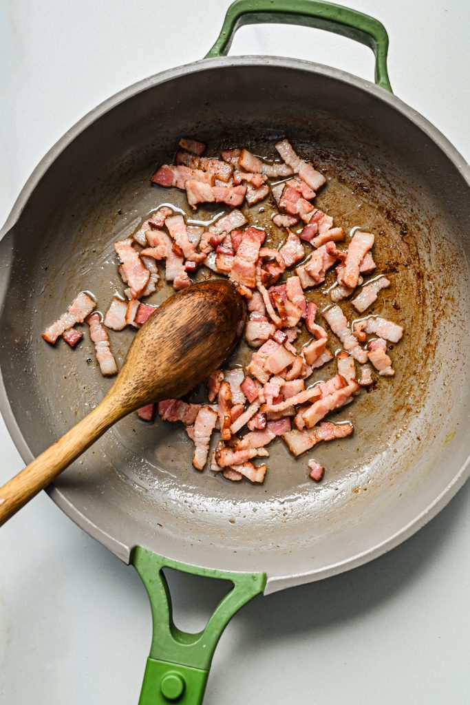 Chopped bacon searing in a skillet.