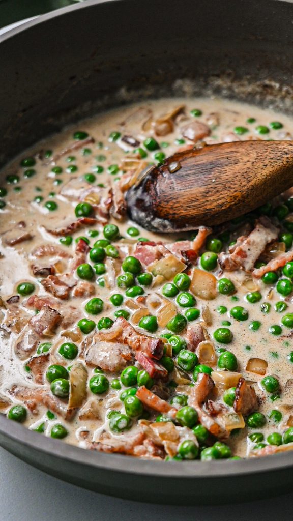 Creamy bacon and pea sauce cooking in a skillet.