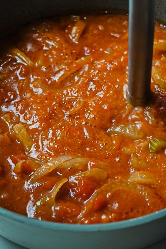 Using an immersion blender to blend the tomato mixture in a skillet.