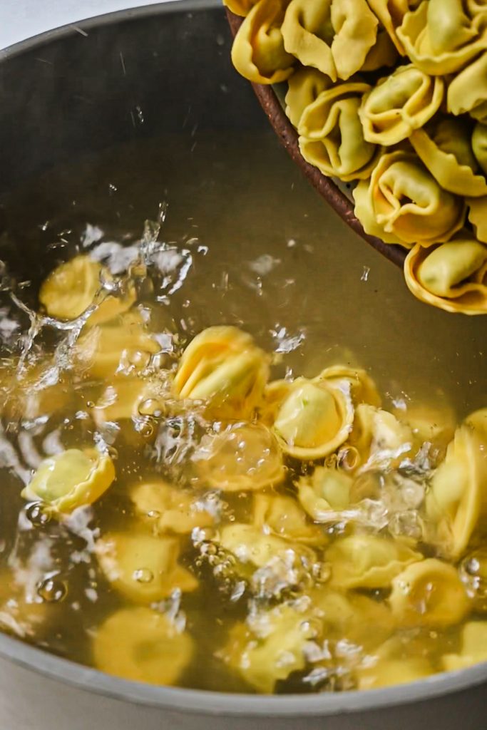 Adding the tortellini pasta into a pot of broth.
