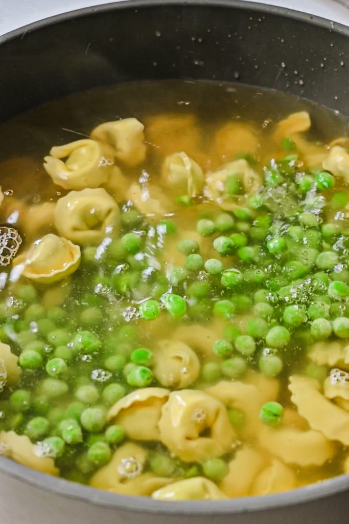 Peas added to the pasta and broth in a pot.
